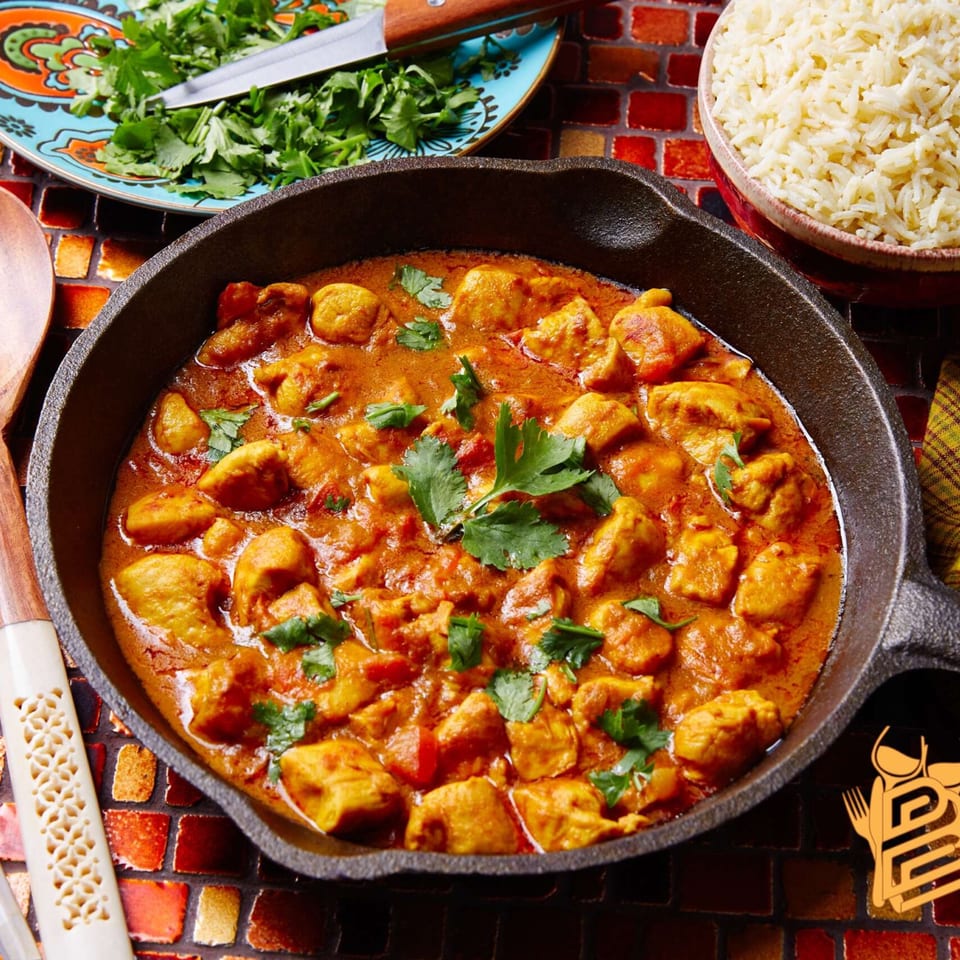Tikka and Grill's chicken curry in a cast iron pan with rice and cilantro.